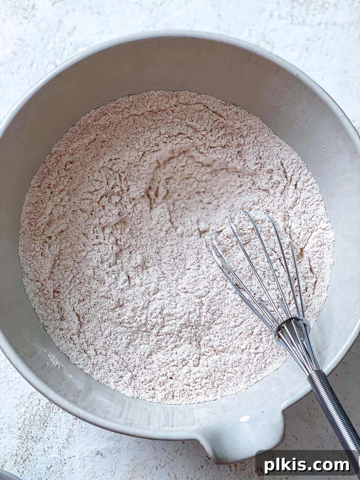 Vegan Churro Bliss 5 Close-up of a hand whisking flour, cinnamon, and salt in a white bowl for vegan churro dough.
