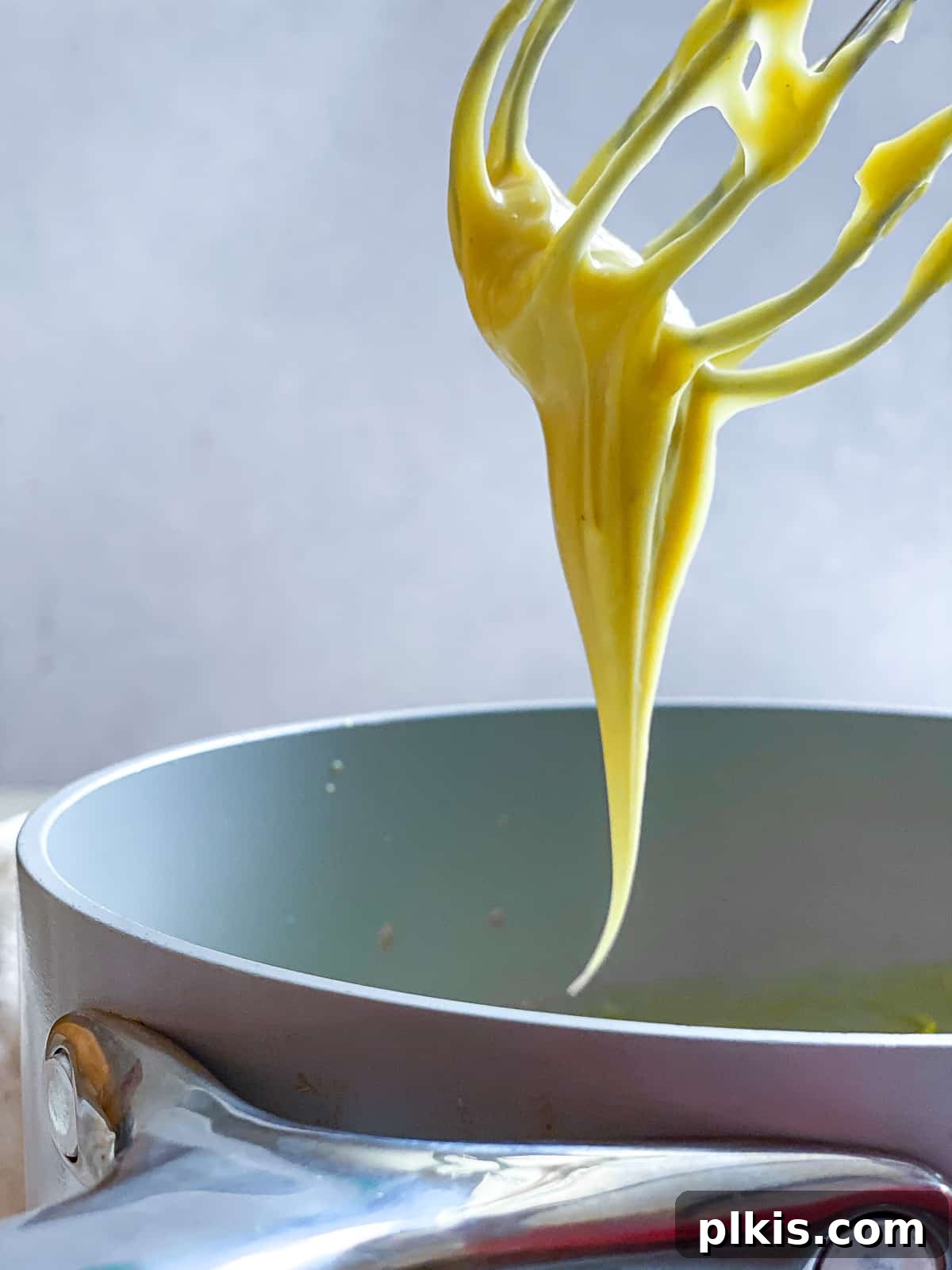 Decadent Vegan Custard 8 Lifting creamy vegan custard out of a grey saucepan with a whisk, showing its texture.