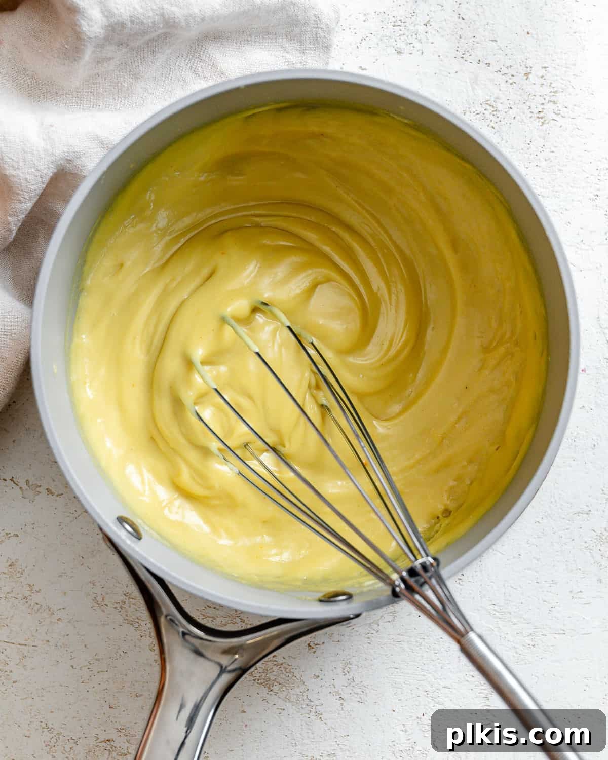 Decadent Vegan Custard 9 Actively whisking vegan custard in a grey saucepan, ensuring a smooth consistency.
