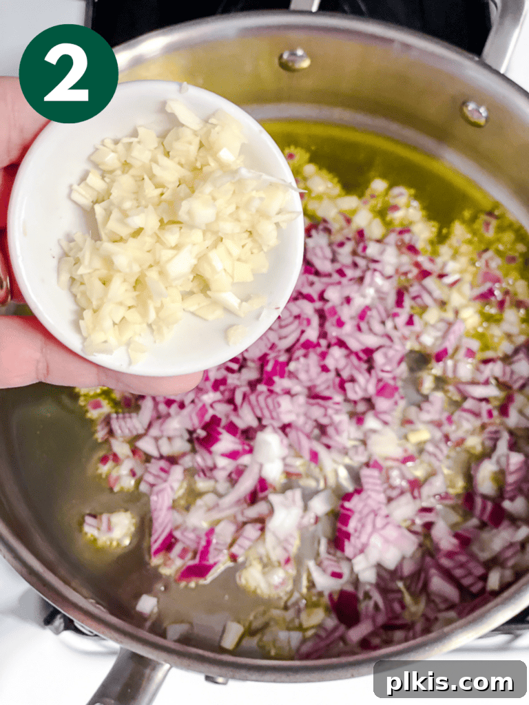 Creamy Plant-Powered Refried Beans 5 Process shot of adding minced garlic to sautéing onions in a pan