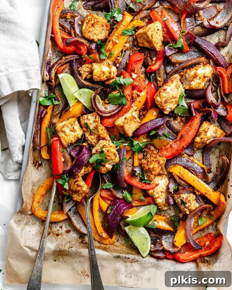 Zesty Tofu Fajita Feast 2 Roasted taco-seasoned tofu chunks, onion, and colorful bell peppers spread on a parchment-lined sheet pan, ready to be cooked to perfection.