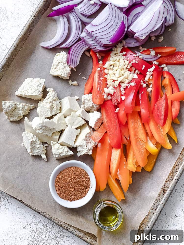 Zesty Tofu Fajita Feast 4 Process shot showing sliced bell peppers, onions, and torn tofu chunks arranged on a parchment-lined baking dish before seasoning.