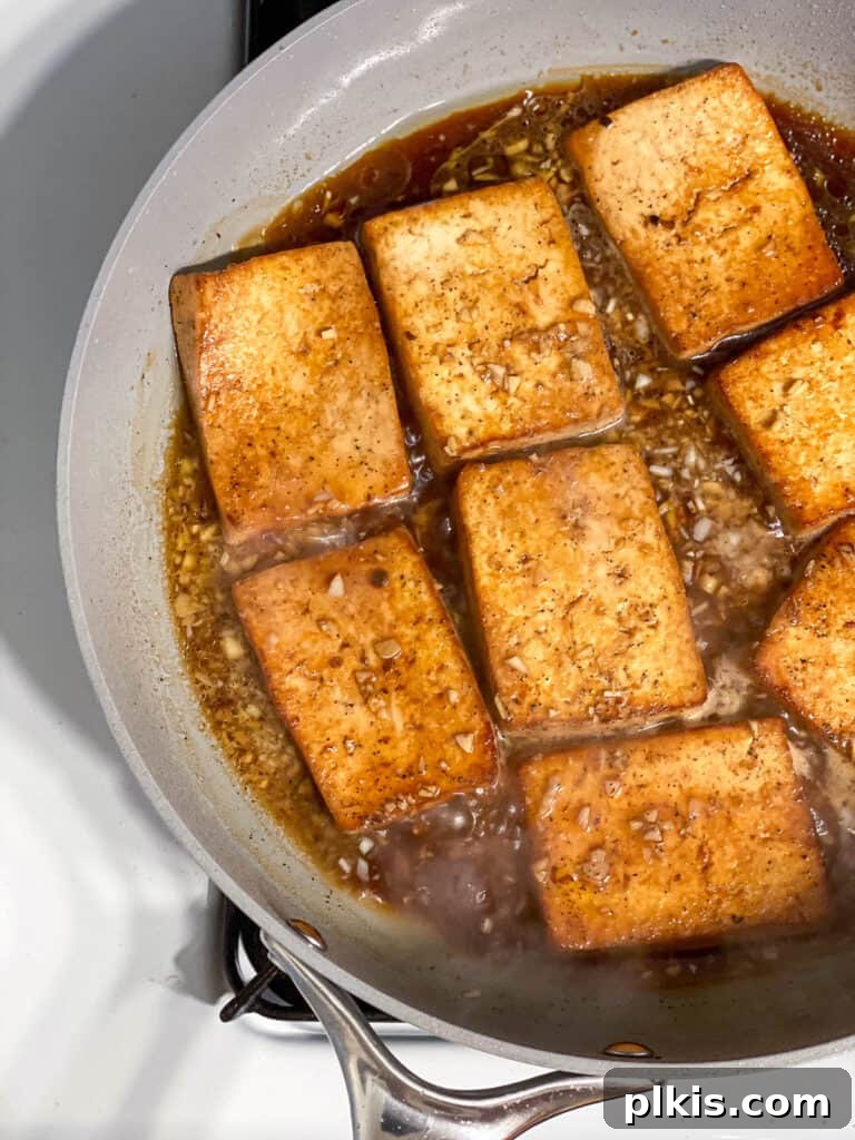 Effortless Tofu Adobo 14 Process shot showing tofu cooking with the marinade simmering on a skillet.