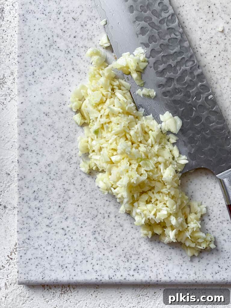 Effortless Tofu Adobo 5 Close-up process shot of slicing garlic on a cutting board.
