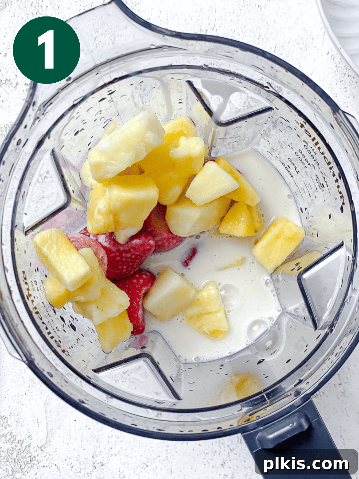 Close-up process shot of ingredients being added into a blender, with plant-based milk at the bottom