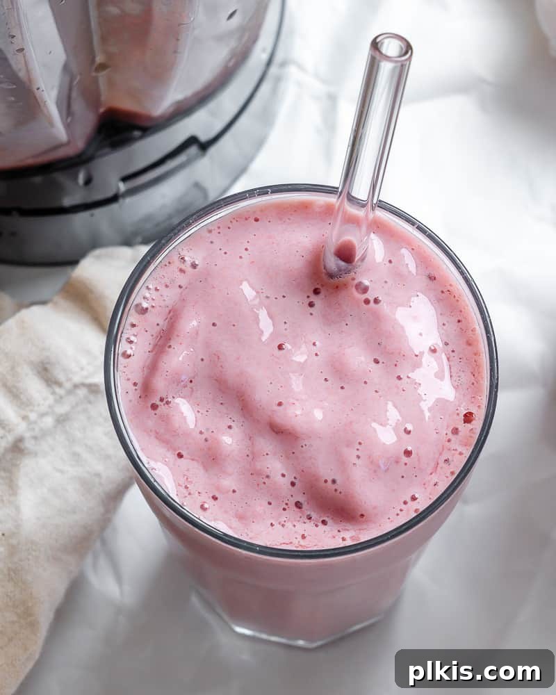 A glass of completed Strawberry and Pineapple Smoothie on a white surface, ready to be enjoyed