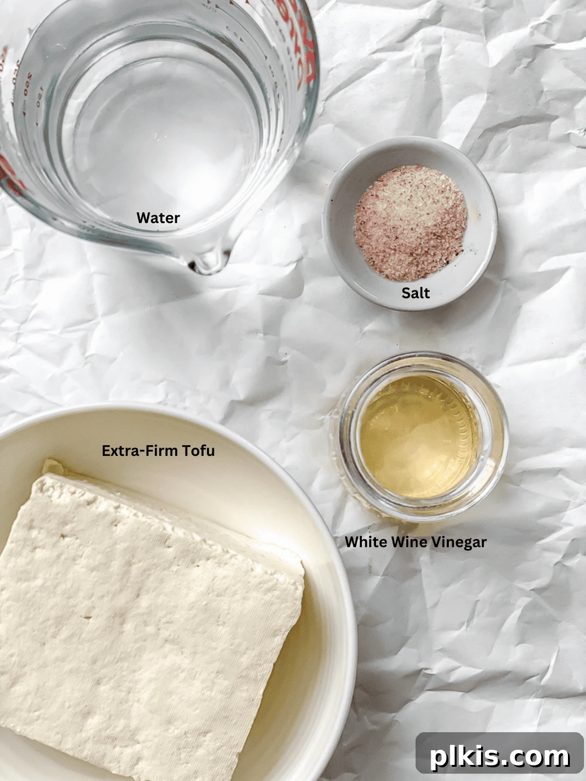 Ingredients for Tofu Feta Cheese laid out on a white surface, including tofu, vinegar, salt, and hot water