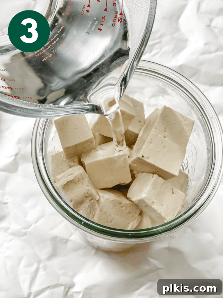 Process shot of hot water being added to the jar with tofu cubes and brine, ready for initial marination