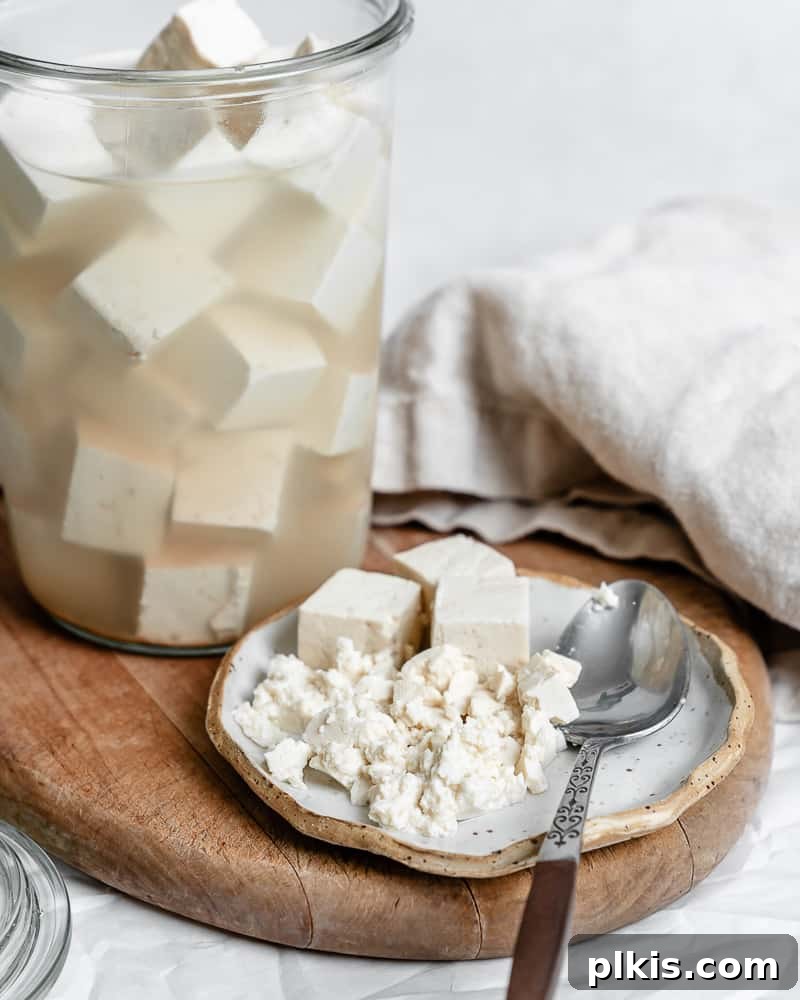 Completed Tofu Feta Cheese presented in a glass jar and a small portion on a plate with fresh herbs