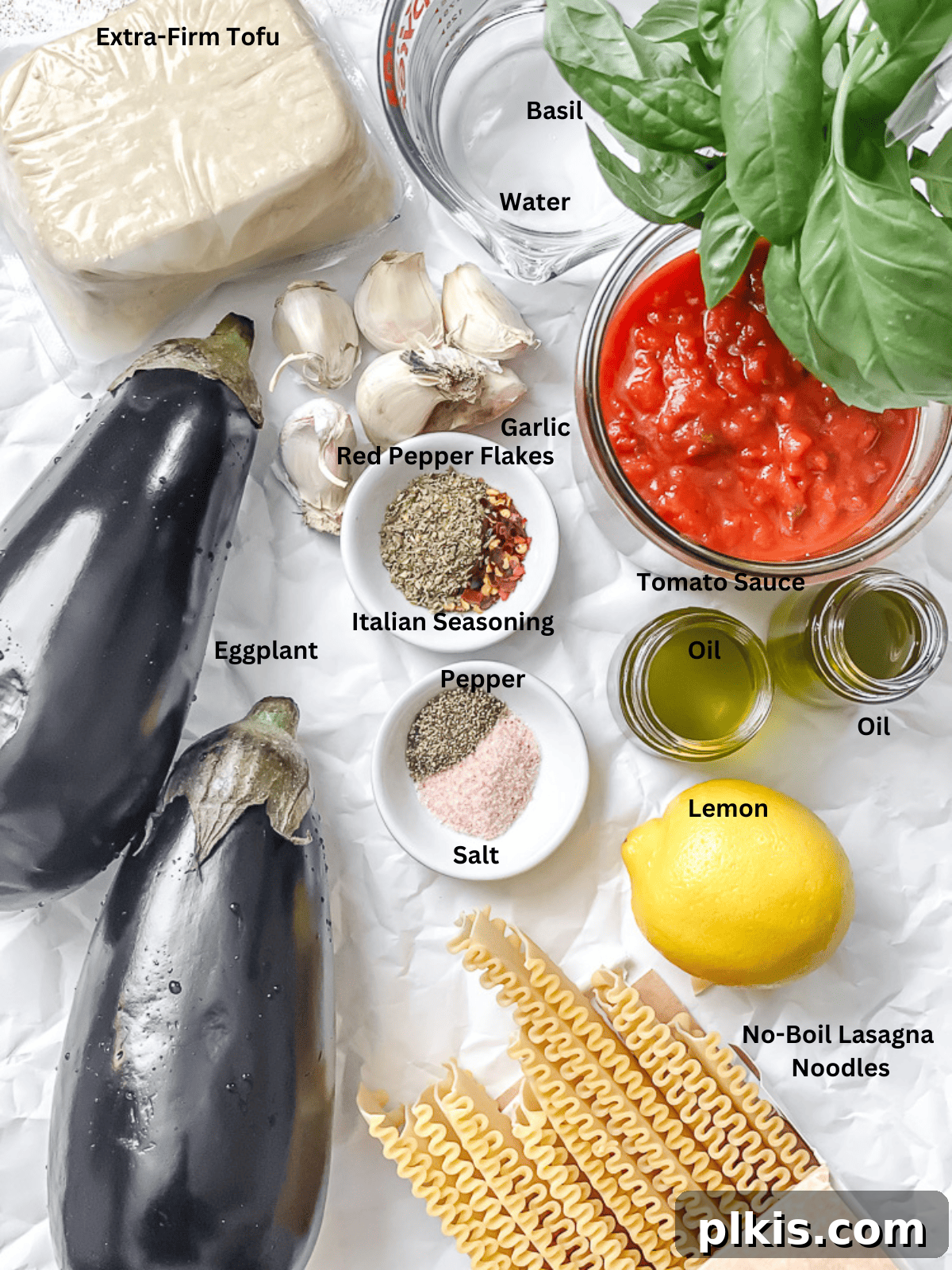 Hearty Vegan Eggplant Lasagna 3 Array of fresh ingredients for vegan eggplant lasagna, including sliced eggplants, a block of tofu, fresh basil, garlic, and jars of tomato sauce, neatly arranged on a white kitchen counter.