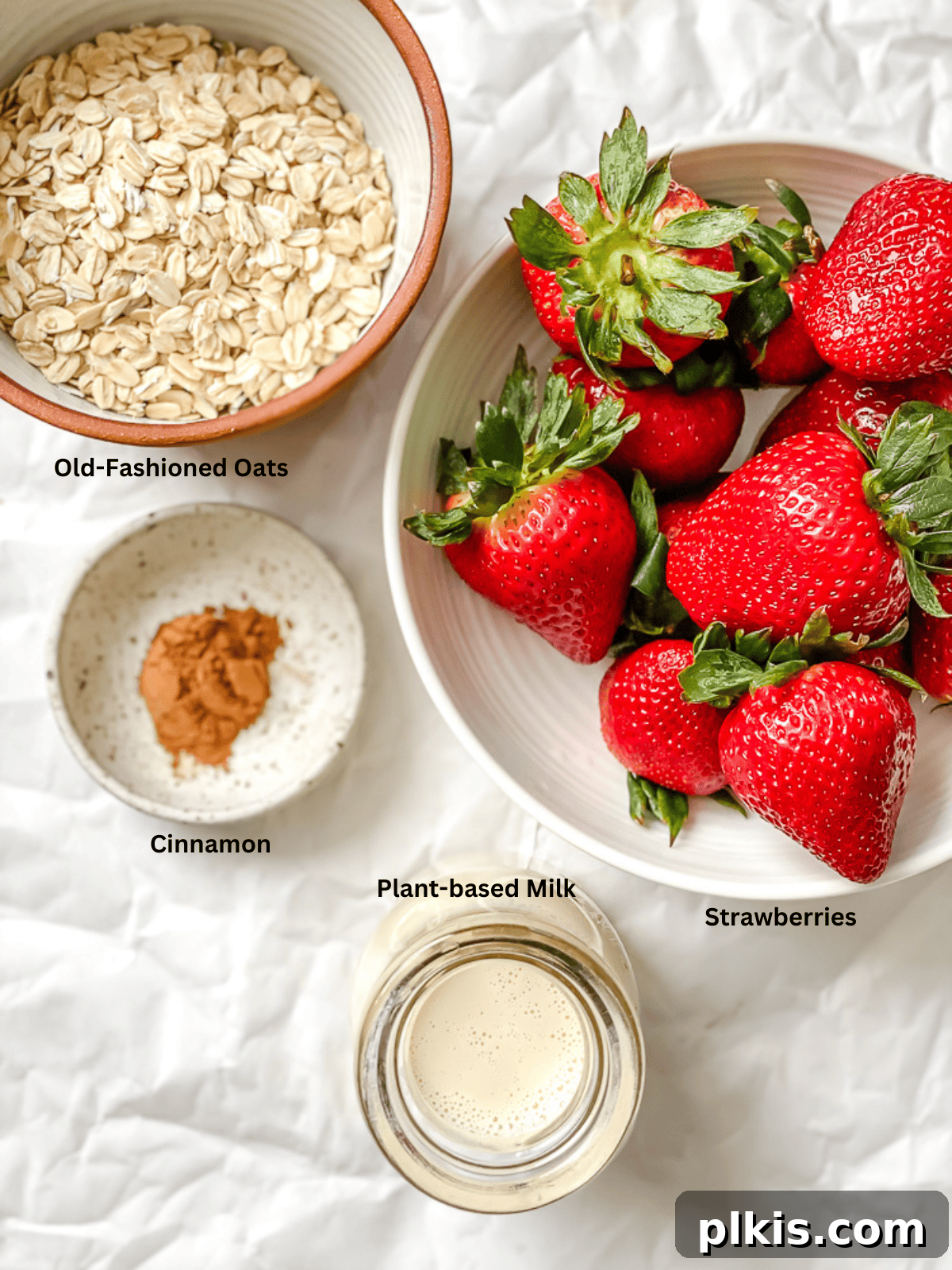 Ingredients for Strawberry Oatmeal measured out on a white surface, including oats, strawberries, and plant milk.