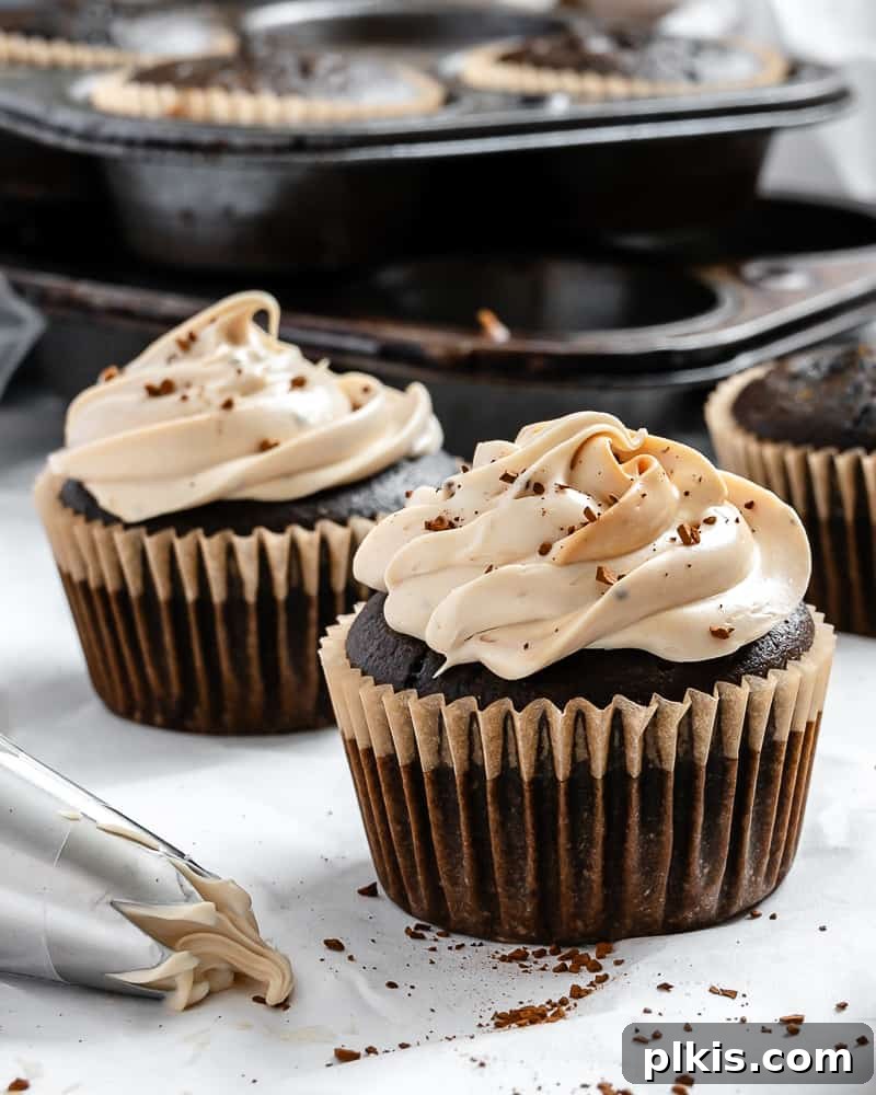Effortless Coffee Cupcakes 11 A close-up shot of a perfectly frosted vegan coffee cupcake, topped with coffee beans, on a white surface.