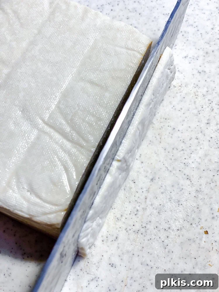 Golden Crispy Tofu Bacon 4 Process shot showing slicing a brick of tofu with a knife into thin strips.