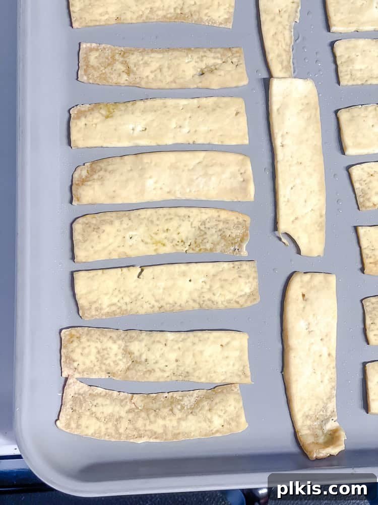 Golden Crispy Tofu Bacon 5 Process shot showing thinly sliced tofu strips arranged on a baking tray.