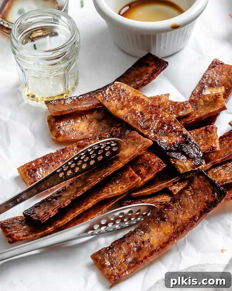 Golden Crispy Tofu Bacon 8 A pile of sauce-covered and baked vegan tofu bacon strips, garnished and ready to serve.