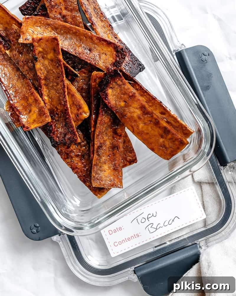 Golden Crispy Tofu Bacon 9 Strips of baked tofu bacon neatly arranged in a clear glass storage container.