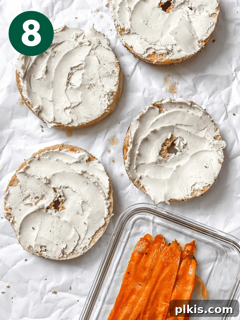 Smoky Carrot Lox 11 A process shot showing delicate carrot lox ribbons being artfully folded and placed on a bagel half generously spread with vegan cream cheese, ready for additional toppings.