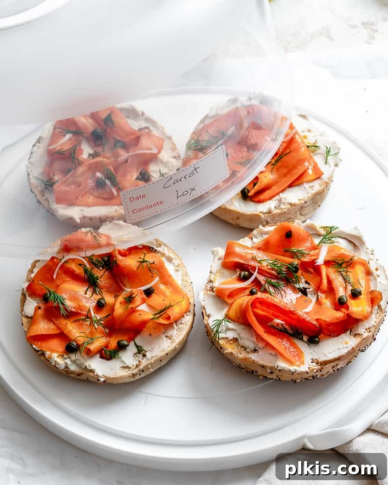 Smoky Carrot Lox 14 Completed Carrot Lox, neatly arranged on bagel halves and placed inside a clear airtight storage container on a white surface, ready for refrigeration.