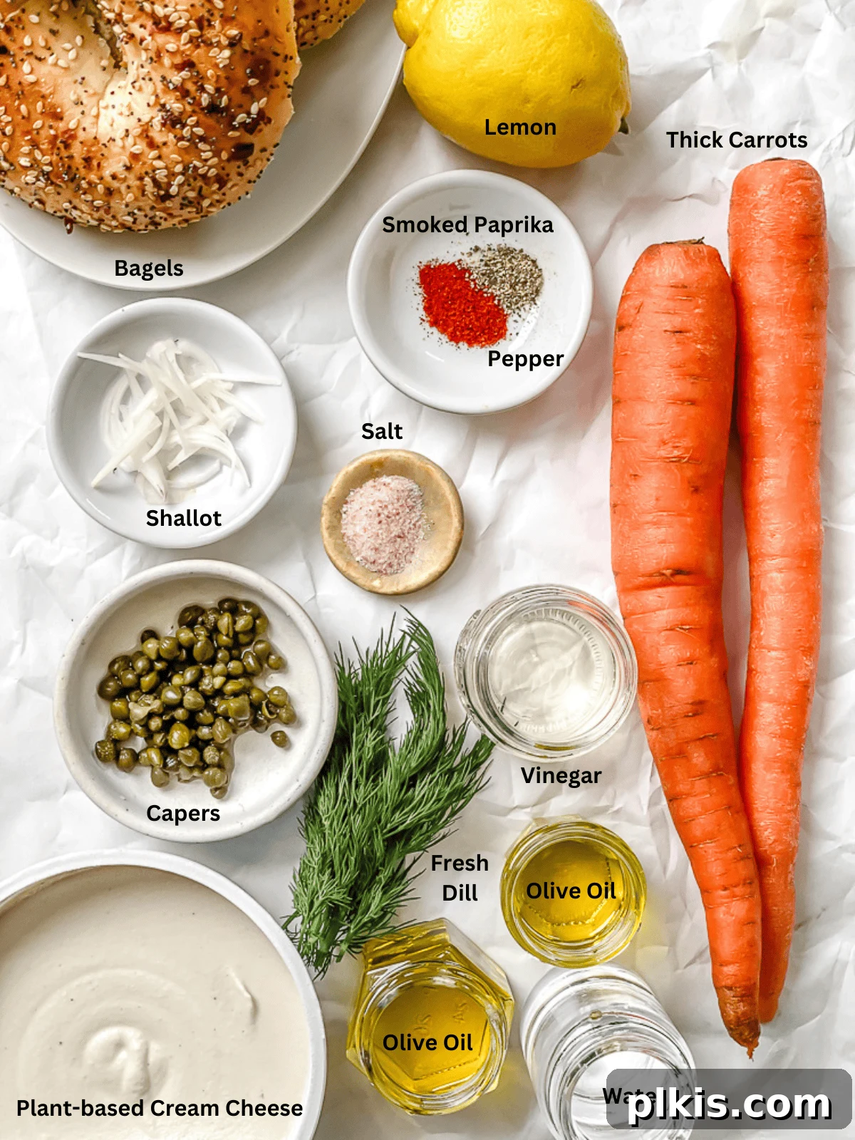 Smoky Carrot Lox 3 A selection of fresh ingredients for Carrot Lox, including whole carrots, olive oil, lemon, rice vinegar, smoked paprika, salt, and black pepper, arranged on a clean white surface.
