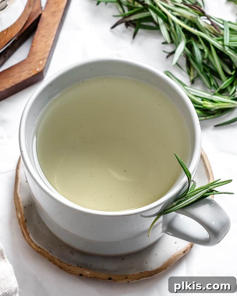 Rosemary's Evergreen Elixir 2 A white mug filled with freshly brewed rosemary tea, garnished with a sprig of rosemary.