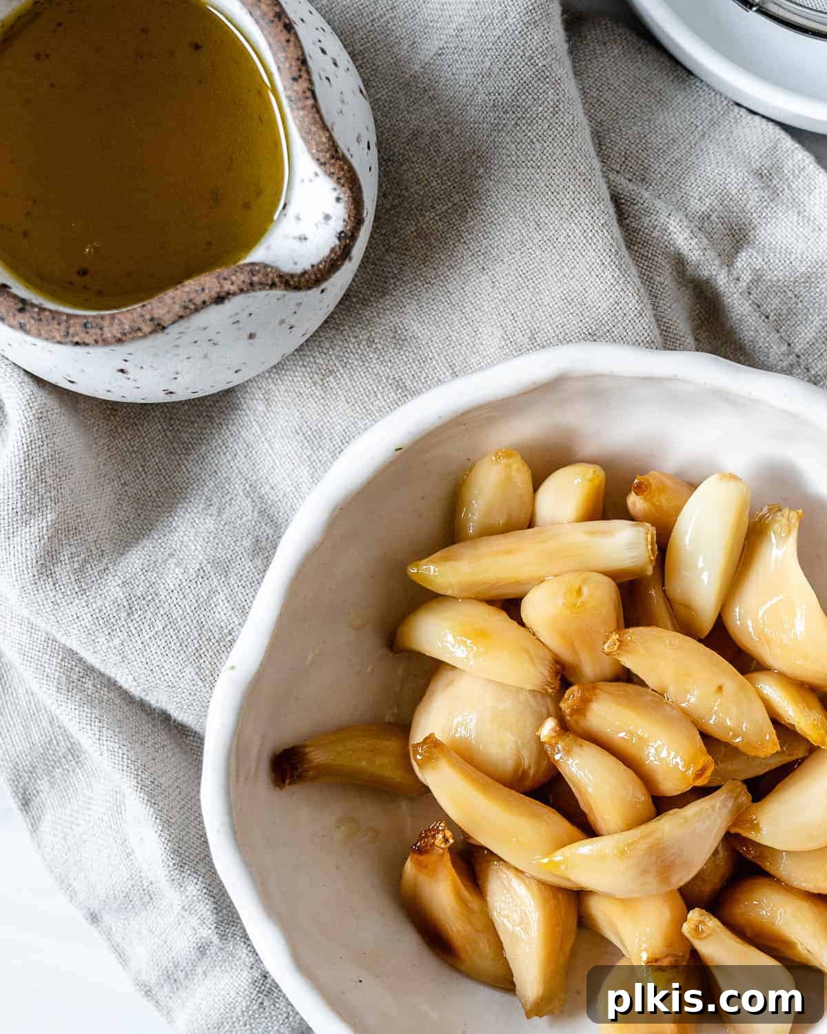 Stovetop Garlic Duo: Pan-Roasted & Confit 2 completed Stovetop Roasted Garlic in a white bowl against a white background with oil in the background