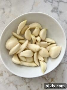 Stovetop Garlic Duo: Pan-Roasted & Confit 4 raw cloves of garlic in a white bowl against a white marble surface