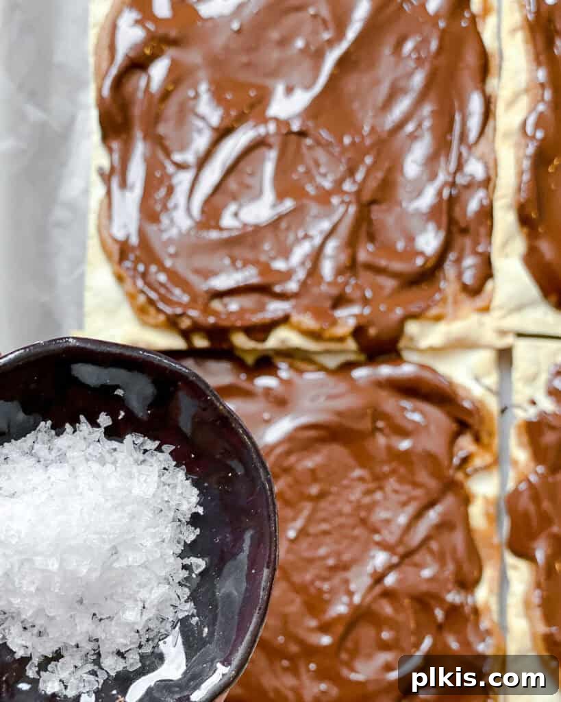 Crispy Matzo Toffee 8 Process shot showing flaky sea salt being sprinkled over the melted chocolate on matzo crackers.