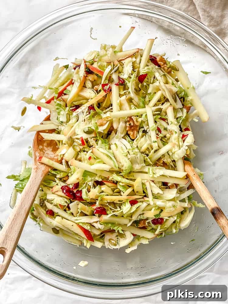 Process shot showing tossing a shaved brussels sprouts salad together with two wooden spoons.