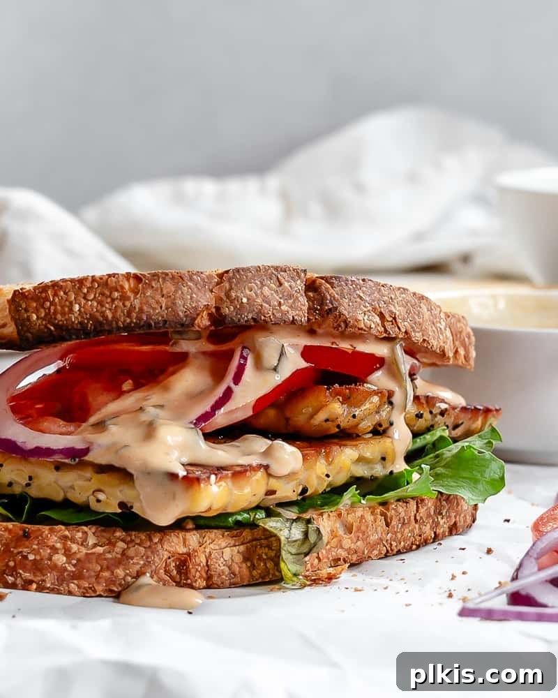 Savory Tempeh Sensation 2 A completed Tempeh Sandwich, cut in half and stacked, showcasing crispy tempeh, vibrant lettuce, and sliced tomatoes, resting on a clean white surface.