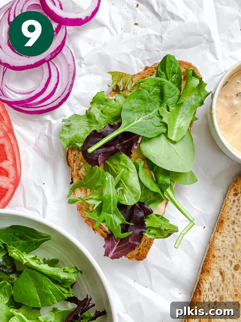 Savory Tempeh Sensation 12 Process shot showing fresh lettuce leaves being placed on a slice of bread already spread with sauce.