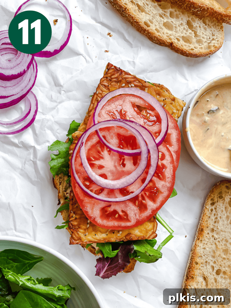 Savory Tempeh Sensation 14 Process shot showing tomato and red onion slices being layered onto the tempeh and lettuce on a sandwich.