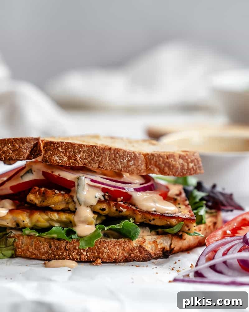 Savory Tempeh Sensation 15 A beautifully assembled Tempeh Sandwich, cut in half, showcasing layers of crispy tempeh, fresh vegetables, and sauce on a white background, ready to be enjoyed.