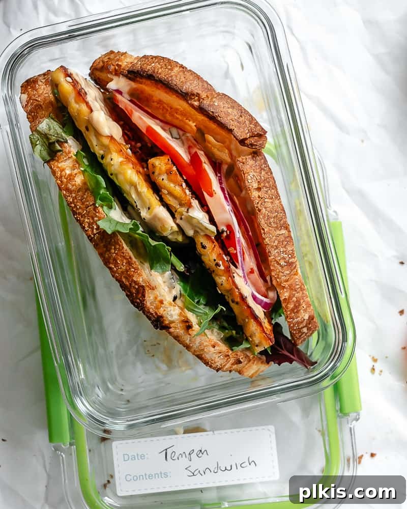Savory Tempeh Sensation 16 A completed Tempeh Sandwich, neatly cut and placed inside a clear rectangular food storage container, ideal for meal prep.