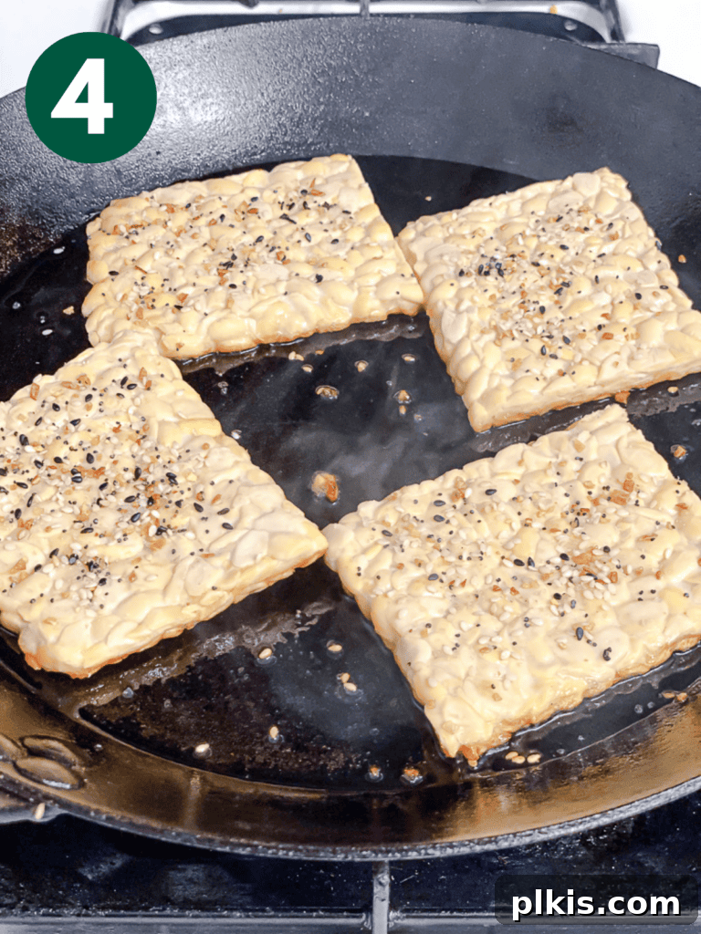 Savory Tempeh Sensation 7 Process shot showing tempeh slices sizzling and browning in a pan with oil and seasoning.