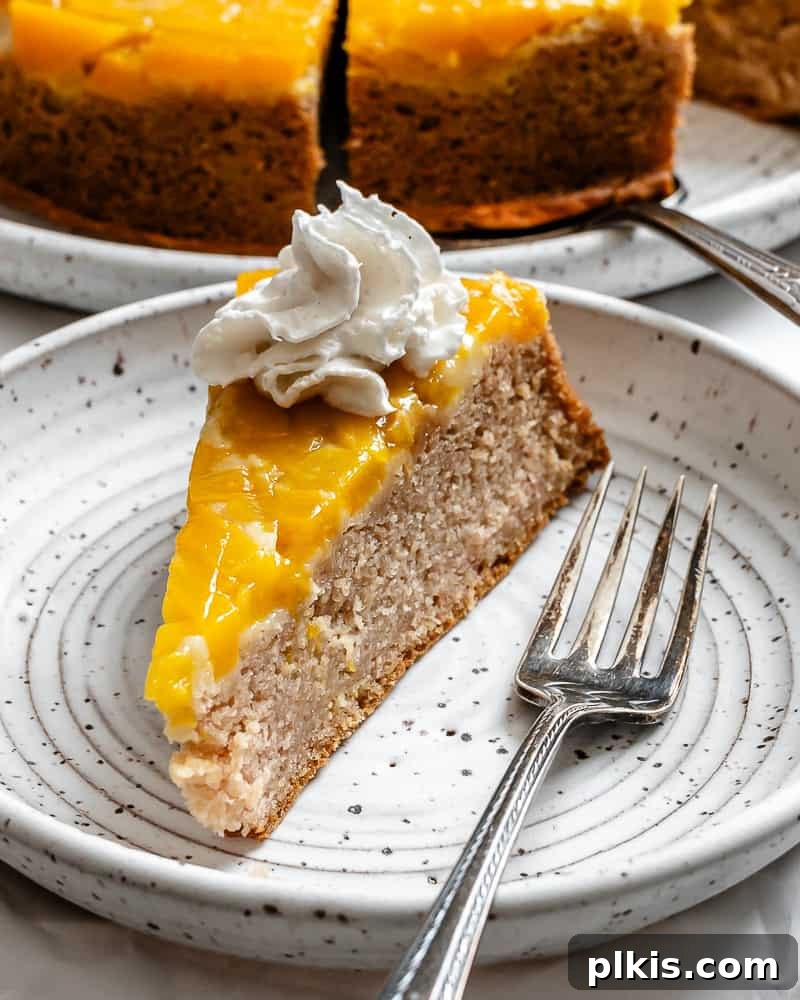 Tropical Mango Delight 17 a slice of mango cake topped with vegan whipped cream on a white plate, ready to be enjoyed.