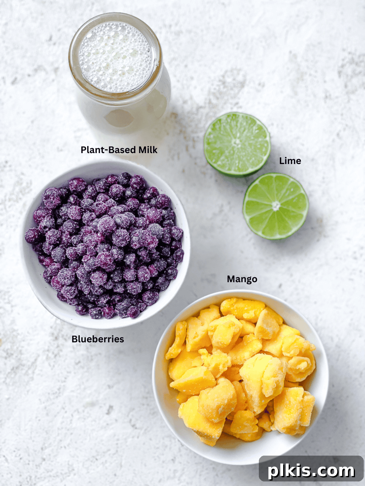 Vibrant Mango Berry Bliss 3 Ingredients for Mango Blueberry Smoothie laid out on a white surface, including frozen fruits and plant-based milk.