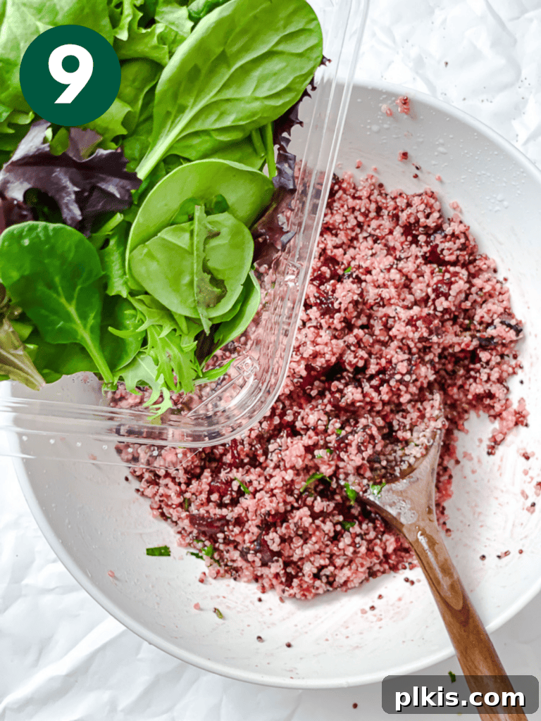 Vibrant Roasted Beet & Quinoa Medley 12 Process shot showing fresh mixed greens being added to the beet and quinoa mixture in a bowl.