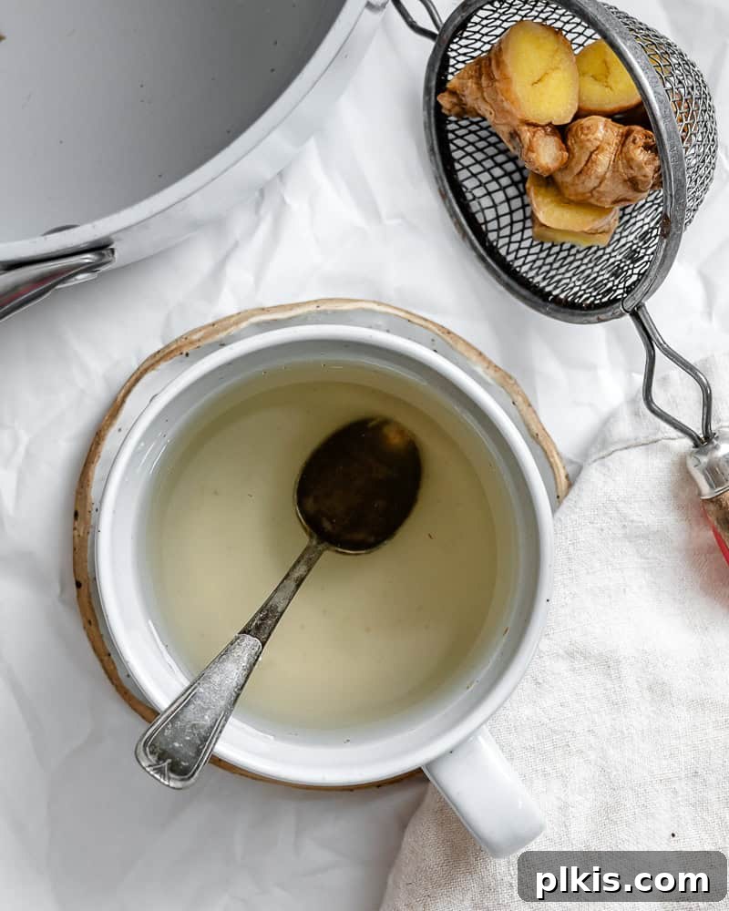 Crafting the Perfect Cup of Ginger Tea 2 A steaming cup of homemade ginger tea with fresh ginger slices on a white background, highlighting its warm and inviting nature.