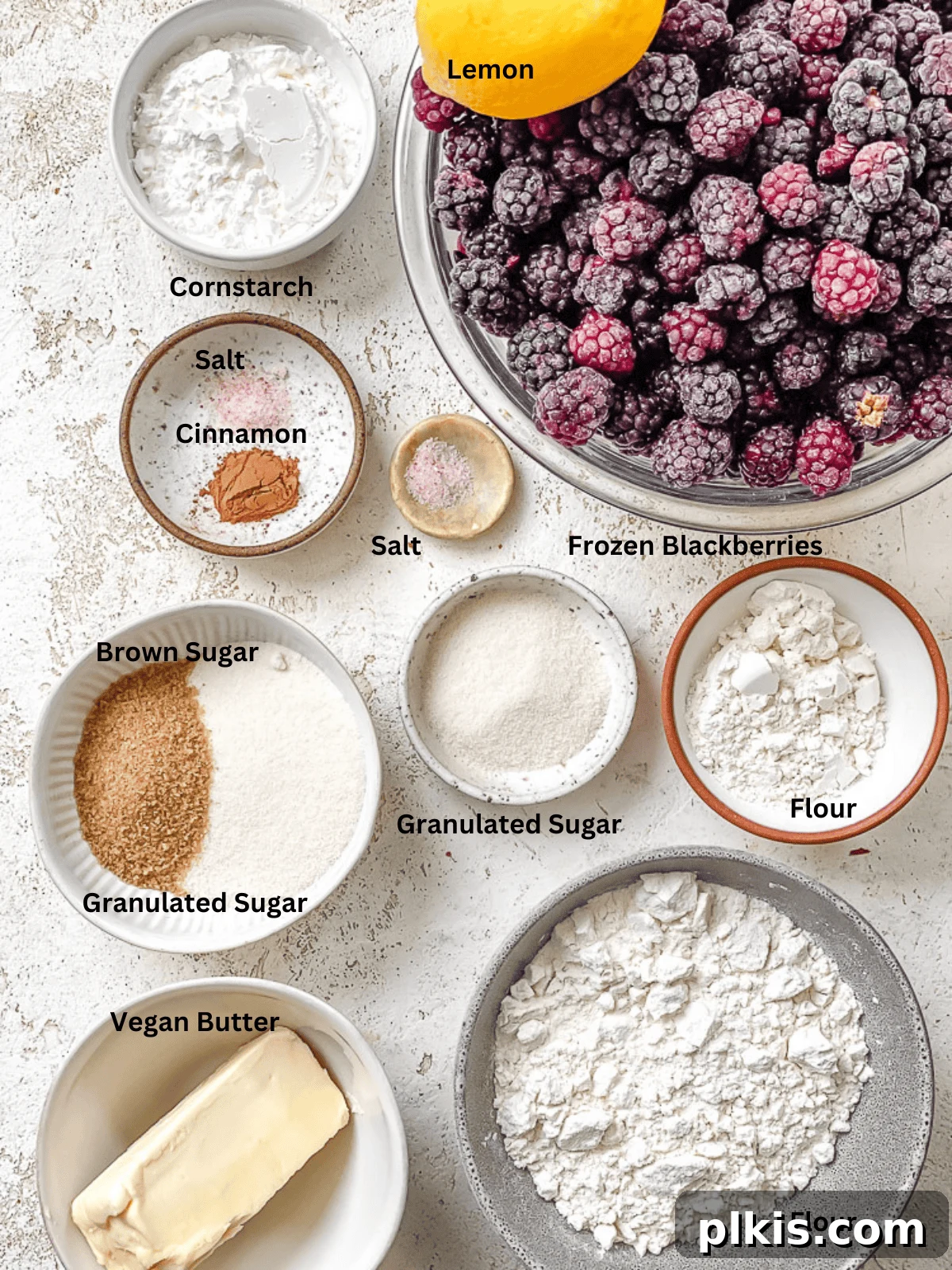 Various ingredients for Easy Vegan Blackberry Crumble laid out on a table, including flour, sugar, vegan butter, and fresh blackberries.