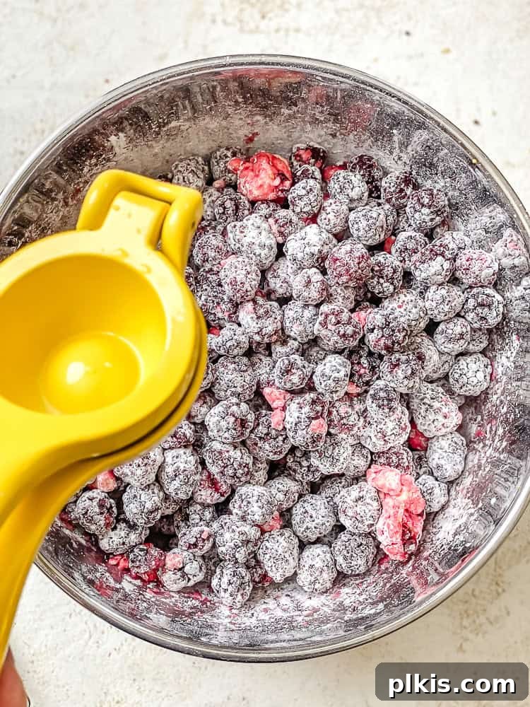 Process shot showing lemon juice being added to a bowl of blackberries and other filling ingredients.