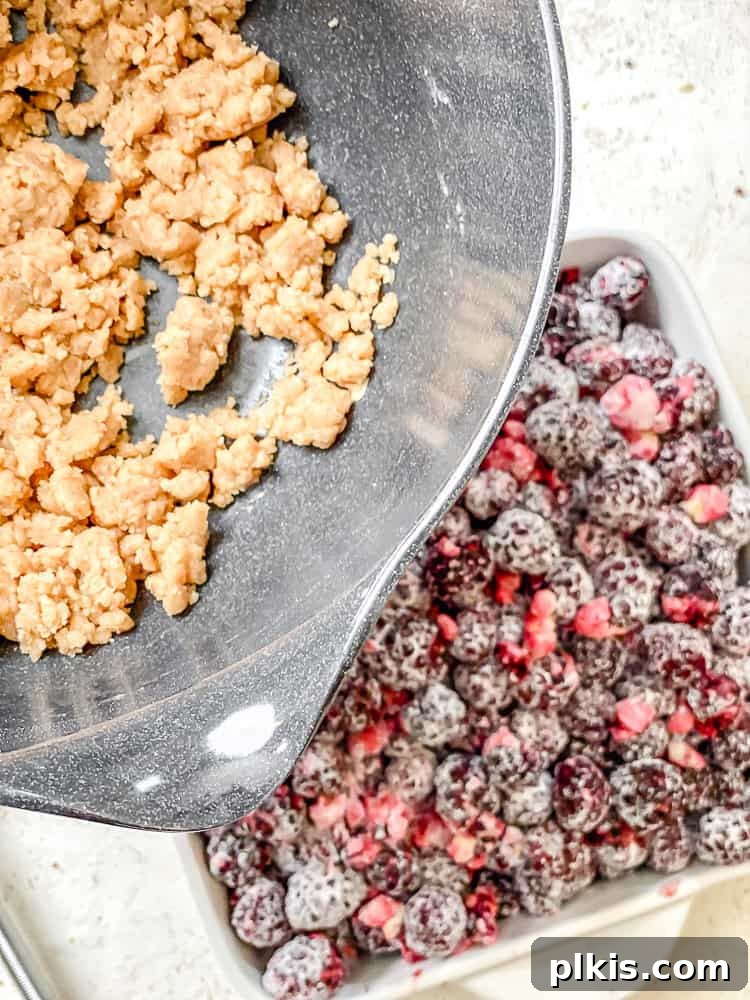 Process shot showing crumble mixture being sprinkled over the blackberry filling in a baking dish.