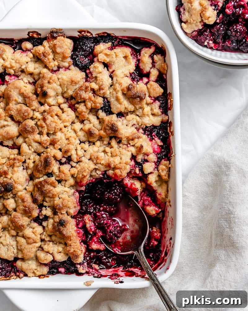 A close-up shot of the completed Easy Vegan Blackberry Crumble in a baking dish, with a serving spoon taking a portion.