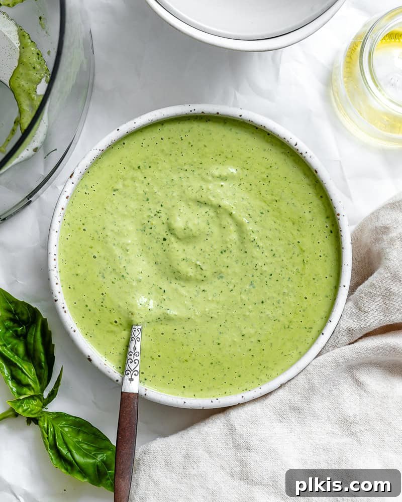 Smooth vibrant green vegan pesto in a white bowl, garnished with fresh basil leaves.