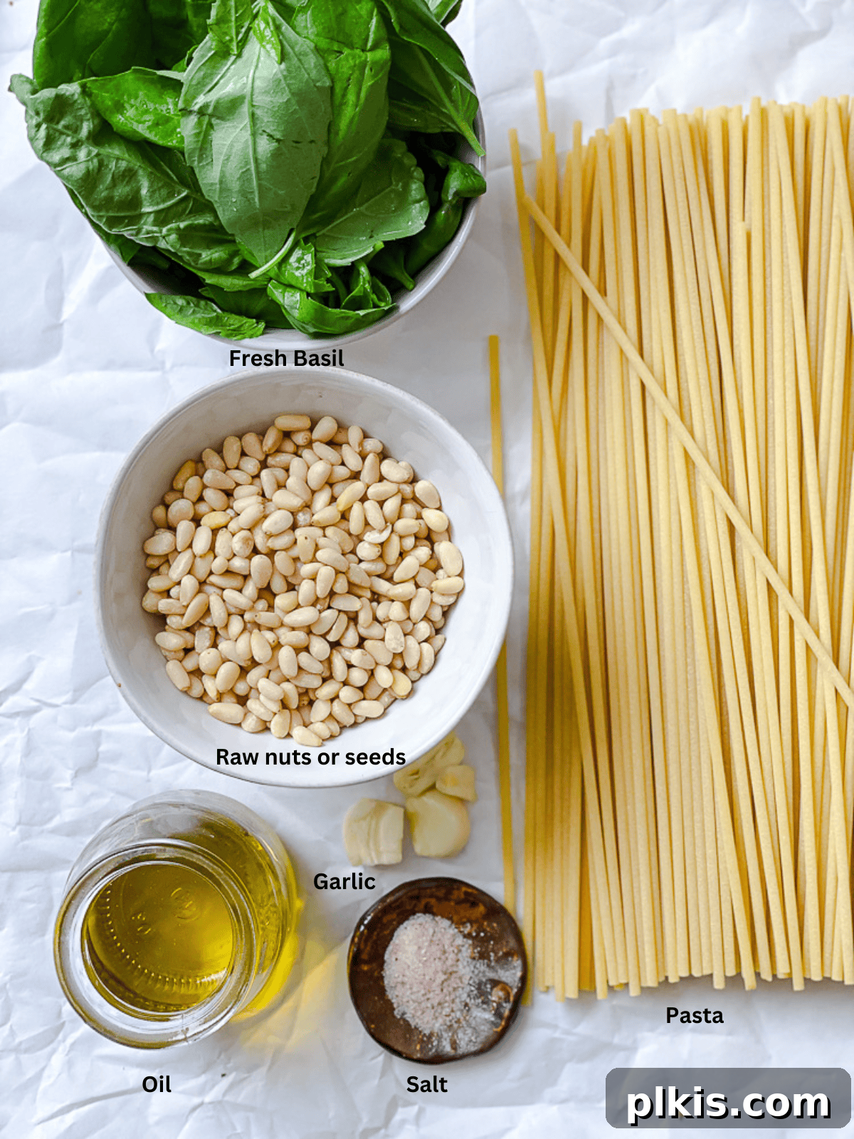 Individual bowls of fresh basil, raw nuts, garlic cloves, and olive oil for vegan pesto.