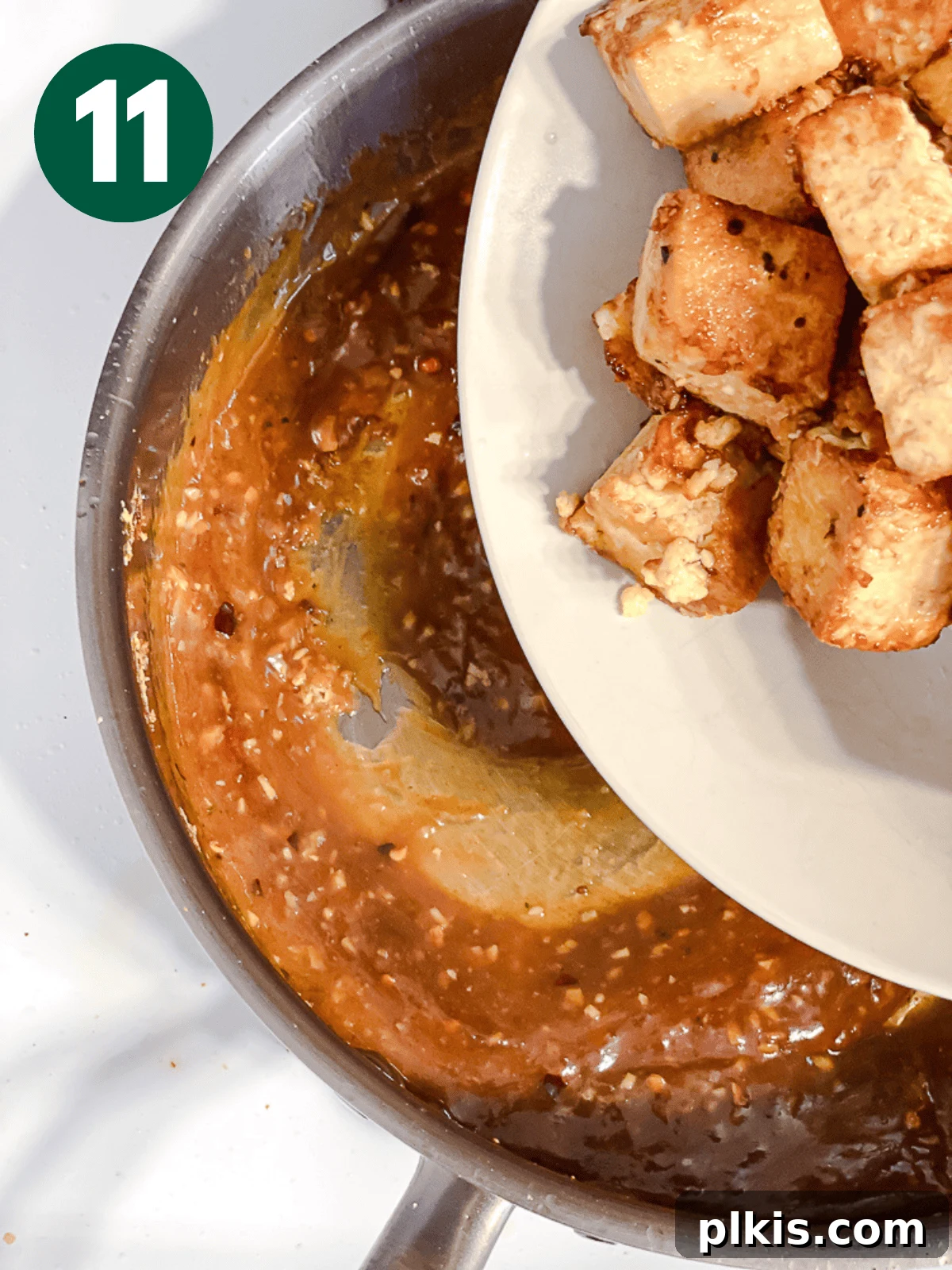 Crispy Tangy Tofu Delight 14 Dumping fried tofu cubes into a large metal pan containing the General Tso's sauce.