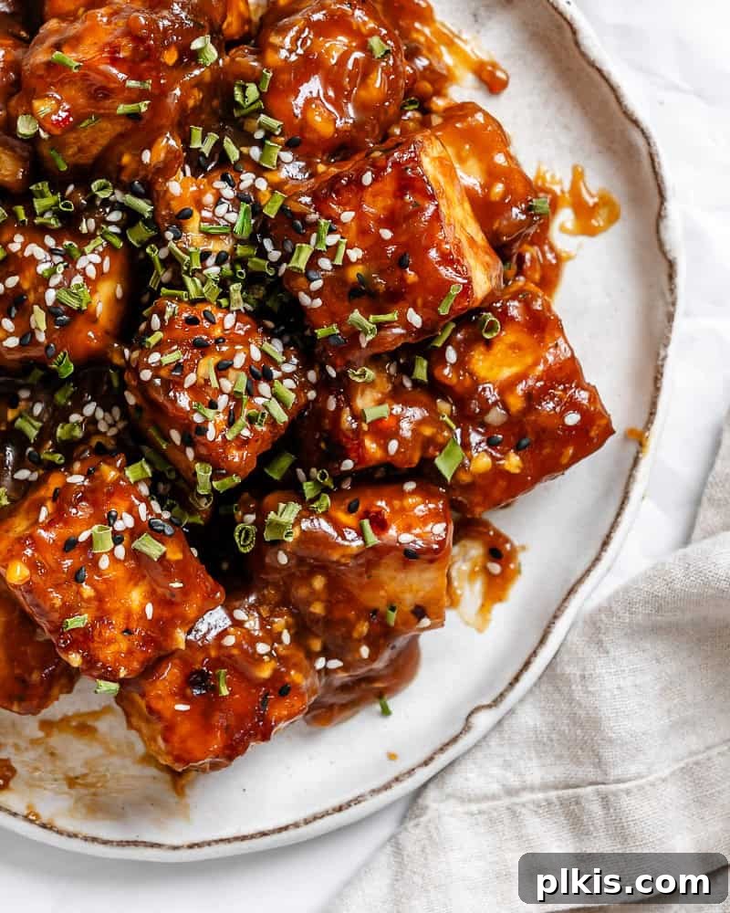 Crispy Tangy Tofu Delight 16 Close-up of General Tso's tofu perfectly coated in sauce on a white plate, garnished with green onions and sesame seeds.