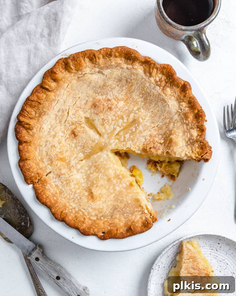 Tropical Vegan Coconut Pineapple Pie 11 A freshly baked Vegan Coconut Pineapple Pie, with a slice already removed, presented in its pie dish against a clean white background.
