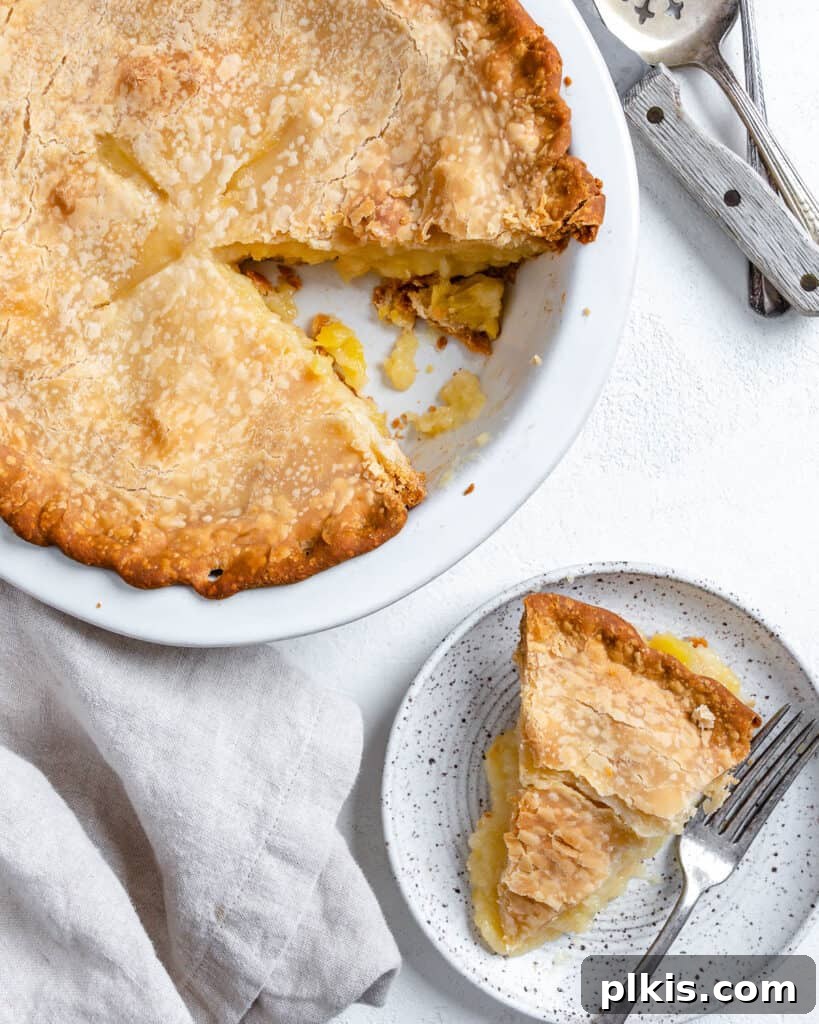 Tropical Vegan Coconut Pineapple Pie 13 A beautifully presented slice of Vegan Coconut Pineapple Pie on a white plate, positioned alongside the remaining pie in its tray, all on a white background.