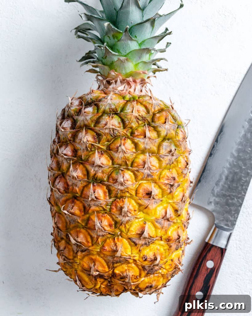 Tropical Vegan Coconut Pineapple Pie 3 A whole, ripe pineapple and a sharp cutting knife are displayed on a white background, signaling the start of the pie-making process.