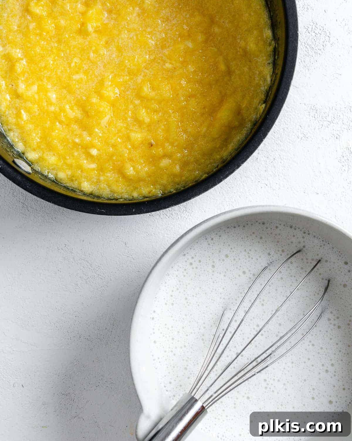 Tropical Vegan Coconut Pineapple Pie 7 The pineapple pie filling mixture simmering in a black saucepan, with a bowl of additional ingredients on the side, against a white background.